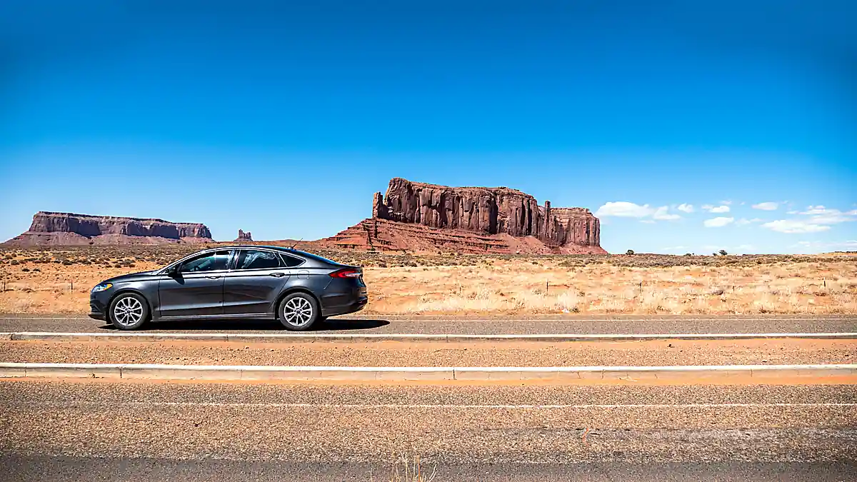 Dunkle Mietwagen-Limousine am Straßenrand vor den Felsformationen des Monument Valley als Sinnbild für die gesamte USA-Route