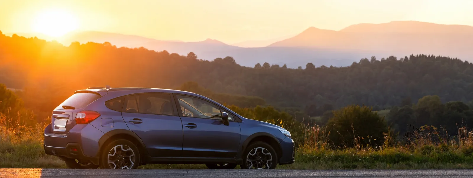 Blauer SUV-Mietwagen vor Bergpanorama bei Sonnenaufgang – der Landweg nach Alaska führt über mehrere Grenzpassagen durch Kanada