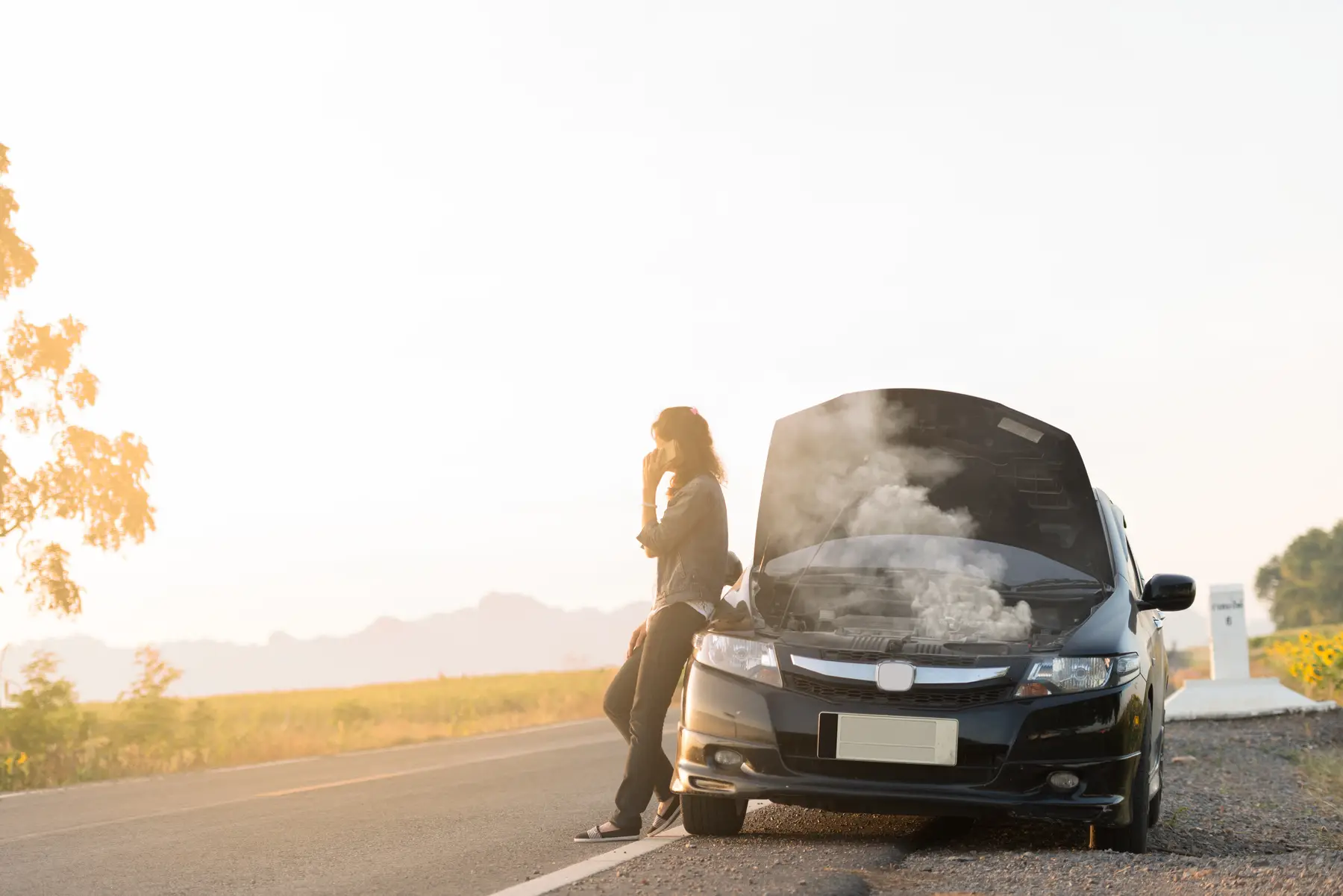 Telefonischer Kontakt zur Roadside Assistance neben einem USA-Mietwagen mit Panne und geöffneter Motorhaube